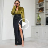 Laura Blair is seen standing in her living room as she films a look book. She wears a pair of large sunglasses with a dark olive satiny shirt and black maxi skirt.