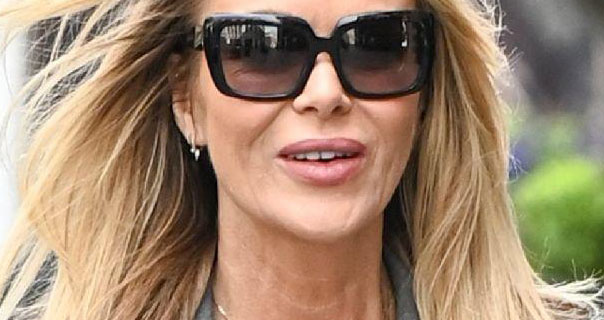Amanda Holden is seen with her loose hair blowing in the wind. She wears a pair of black frame sunglasses with small silver earrings and a dark nude lipstick.