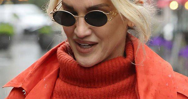 Ashley Roberts wears sunglasses in the rain. She appears in a turtleneck orange knitted jumper and an orange trench coat.
