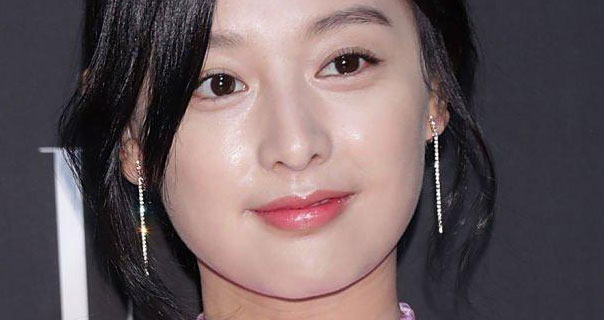 Kim Ji-won smiles slightly. She appears in front of a grey and white background. She wears her hair back with a pair of silver dangling chain earrings and pink lipstick.