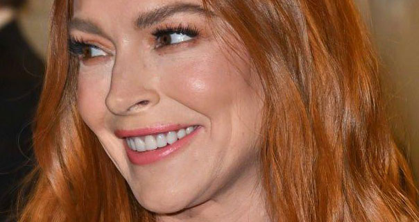 Lindsay Lohan smiles and turns to the side. She wears her hair down with a light pink matt lipstick.