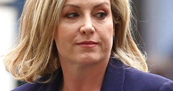 Penny Mordaunt glances to the side. She has her light blonde hair loose and wears a dark pink lipstick. Penny is seen in a dark purple blazer.