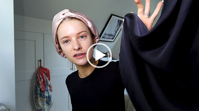 Victoria Magrath sits in her dressing room at home. She wears her hair up and in a pink hair turban with no makeup. Victoria holds up the black slip dress she is going to change into.