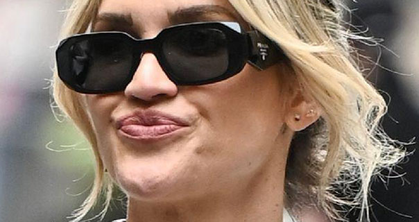 Ashley Roberts purses her lips as she looks to one side. Her blonde hair is tied up with strands framing her face. She wears a pair of black blocky sunglasses.