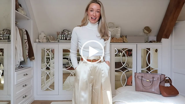 Josie Irons stands her dressing room at home. She is seen in a light cashmere roll neck top and a pair of cream satin trousers. She appears in front of white stencil mirror cabinets, white draws and exposed wooden beams.