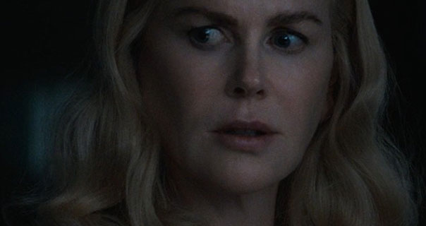 Nicole Kidman is seen with her blonde hair down and curled. She glances to one side and looks a concerned. Nicole stands in a very dark room.