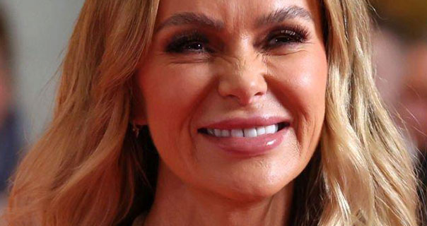 Amanda Holden smiles and looks into the camera. She wears her thick blonde hair loose and in waves. Amanda appears in a plumping dark pink lipstick and black mascara.