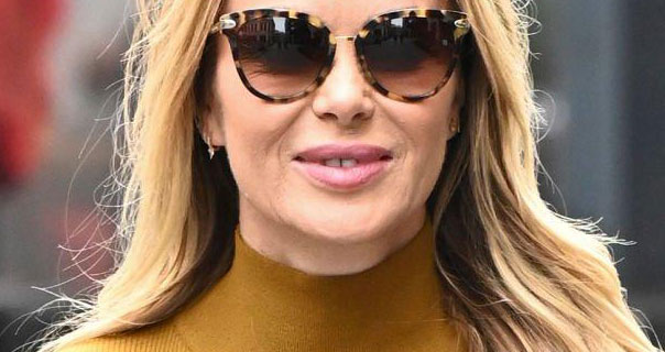 Amanda Holden appears with her thick blonde hair straight and down around her shoulders. She wears a pair of large sunglasses and a dark mustard top.