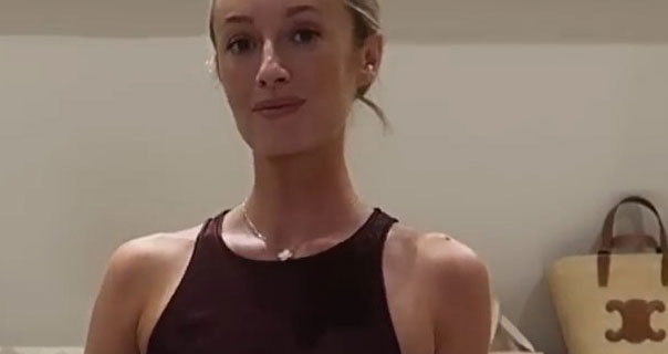 Josie Irons stands in the dressing room area of her home in the Cotswolds. She wears a dark burgundy sleeveless dress with a gold cross necklace. Josie appears with her hair tied back and up.