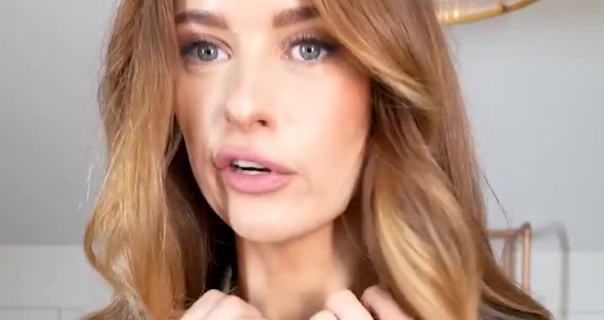 Victoria Magrath appears with her blonde and brown hair down and a little curled. She wears a matte pink lipstick as she films in a cream and rose gold room at her home.