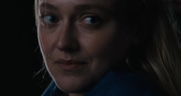 Dakota Fanning looks to the side. She sits outdoors on a dark night. Her blonde hair is loose and pushed back. Dakota wears a blue robe and a dark pink lipstick.