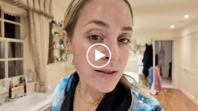 A close-up of Fleur De Force after applying a Qure Skincare facial. Fleur turns her face in the light. She stands in a white and light wood floor bathroom at her home. Fleur wears a start design navy and blue mix pyjama top with her hair tied back in a ponytail.