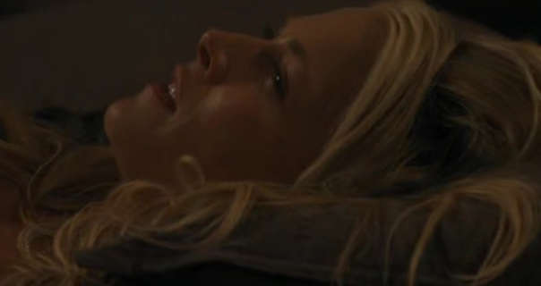 Ali Larter lies on a dark grey pillow. Her long blonde hair spreads out around her. She wears a red lipstick and mascara in a dark bedroom.