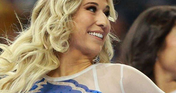 A Detroit Lions cheerleader wears her long blonde hair down and curled. She performs in a sheer white top with a blue Lions logo on it.