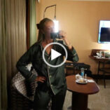 Josie Irons stands in a hotel room as she ends her evening. She holds her vlogging camera in one hand as she records through a full length mirror. Josie wears a pair of dark green pyjamas that have a white piping and buttons.