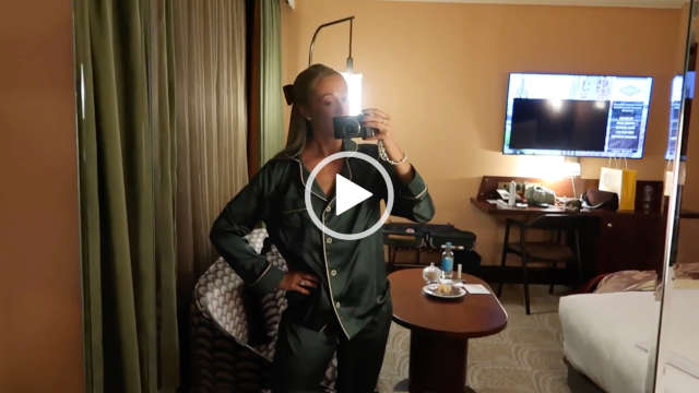 Josie Irons stands in a hotel room as she ends her evening. She holds her vlogging camera in one hand as she records through a full length mirror. Josie wears a pair of dark green pyjamas that have a white piping and buttons.