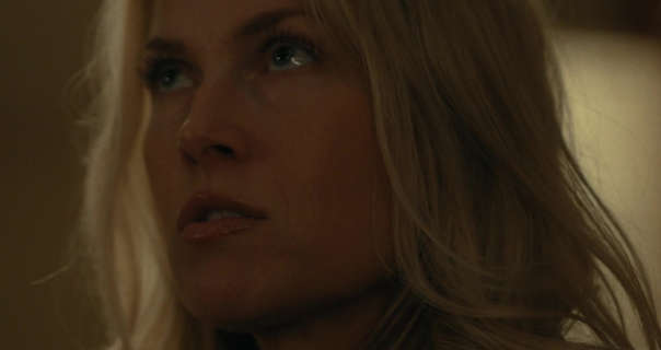 Ali Larter looks up. She appears in a bedroom with light hitting closed blinds behind her. Her blonde hair is loose and messy and she is seen in a pink gloss lipstick.