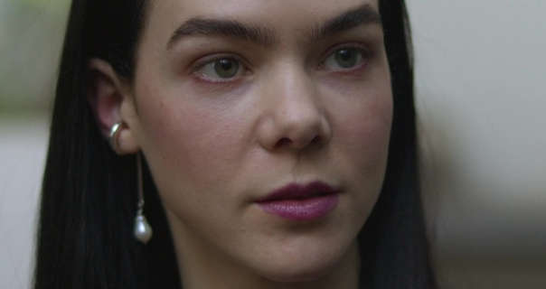 Ximena Lamadrid is seen with her long black hair down and pushed back. She wears a dark pink lipstick with a pair of pendant pearl earrings in an episode of Bandidos.