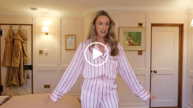 Josie Irons stands with her arms down by her side and slight outstreached. She wears a pair of light pink traditional pyjamas that have a dark pink stripe design. Josie has her blonde hair down in loose curls. She stands in a white, cream and exposed wood bedroom in her home during a Fashion Mumblr vlog.