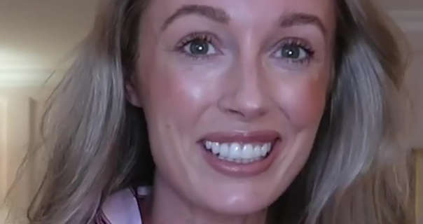 Josie Irons smiles as she stands in one of her filming rooms in her Cotswolds house. Her hair is tousled and loose. She wears bright blush and a dark pink gloss lipstick.